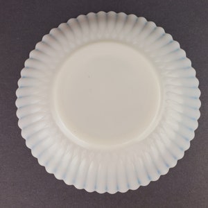May include: A white milk glass plate with a blue scalloped edge. The plate has a fluted design.