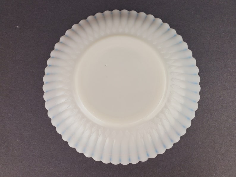 May include: A white milk glass plate with a blue scalloped edge. The plate has a fluted design.