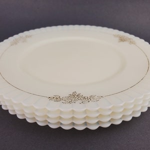 May include: A stack of four white glass plates with a scalloped edge and a gold floral design around the rim.