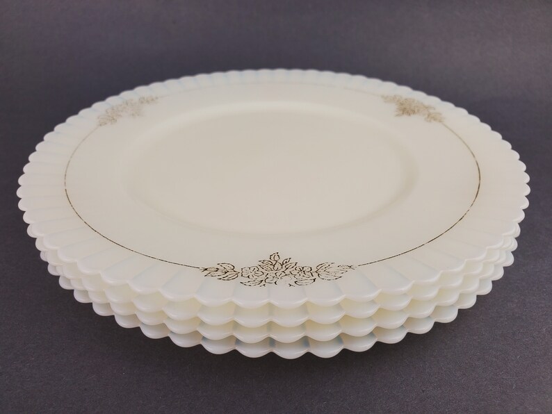 May include: A stack of four white glass plates with a scalloped edge and a gold floral design around the rim.