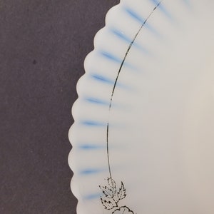 May include: A white ceramic plate with a scalloped edge and blue and black floral design. The plate has a white background with blue stripes and a black floral design.