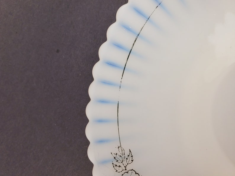 May include: A white ceramic plate with a scalloped edge and blue and black floral design. The plate has a white background with blue stripes and a black floral design.