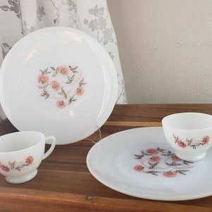 May include: A set of three white ceramic plates with a floral design in shades of pink and brown. The plates are on a wooden surface.