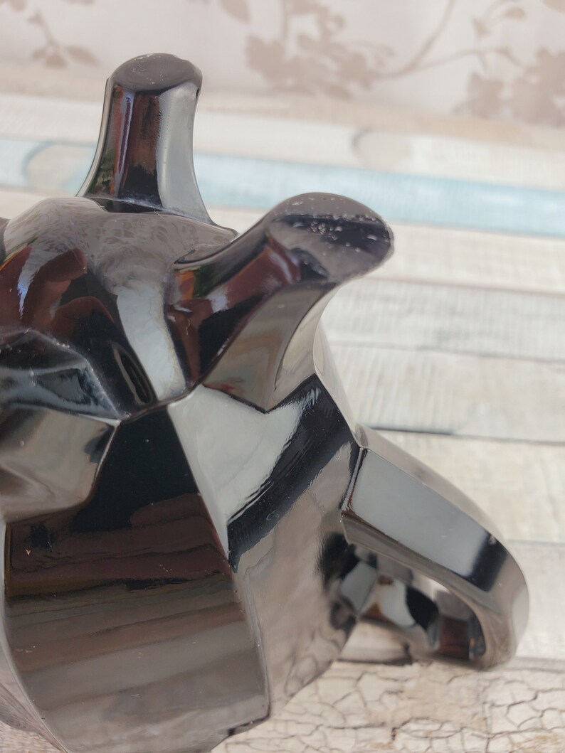 K&ouml;nnte beinhalten: Eine schwarze Glasteekanne mit geometrischem Design. Die Teekanne hat einen Griff und einen Ausguss. Die Teekanne ist aus gl&auml;nzendem, reflektierendem Material.