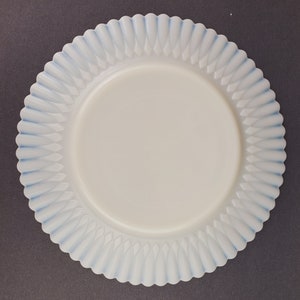 May include: A white milk glass plate with a blue scalloped edge. The plate has a raised design of small, pointed leaves.