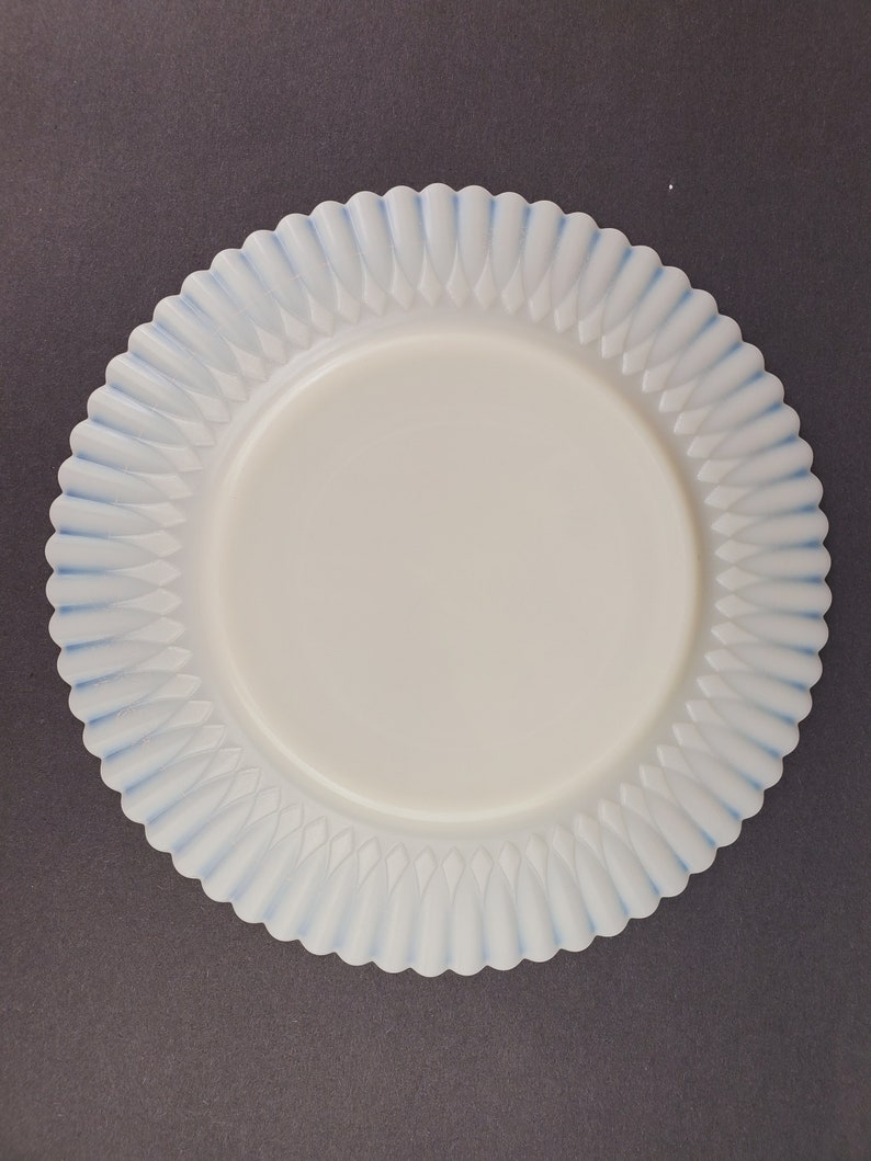 May include: A white milk glass plate with a blue scalloped edge. The plate has a raised design of small, pointed leaves.