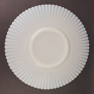K&ouml;nnte beinhalten: Ein wei&szlig;er Milchglasteller mit blauem Rand und einem gewellten Rand. Der Teller hat ein geriffeltes Design.