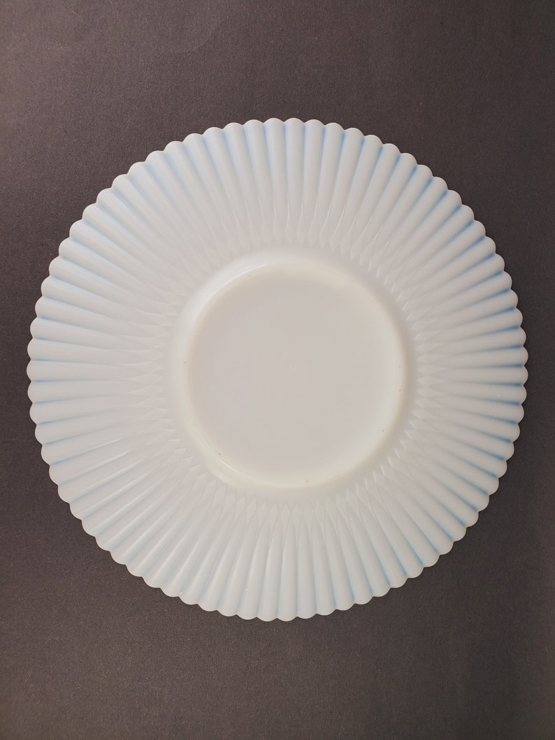 K&ouml;nnte beinhalten: Ein wei&szlig;er Milchglasteller mit blauem Rand und einem gewellten Rand. Der Teller hat ein geriffeltes Design.