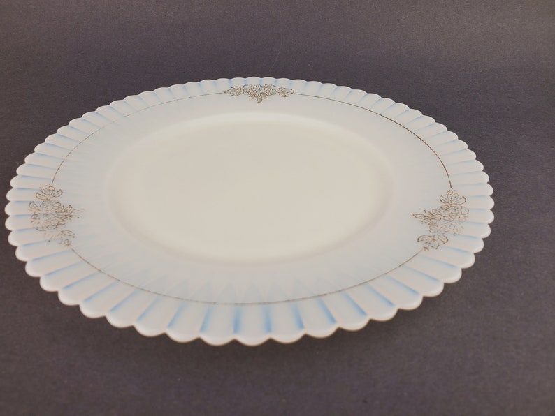 May include: A white glass plate with a scalloped edge and a blue and gold floral design.