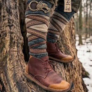 Peut inclure: Bottes à lacets en cuir marron avec bouts beiges, portées avec des bandes molletières en laine grise maintenues par des rubans en tissu à motifs marron et une boucle métallique en forme de dragon. Un pendentif rectangulaire gravé est suspendu.