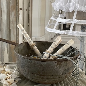 May include: A vintage metal colander with rolled up sheet music inside. The colander is sitting on a white lace tablecloth.