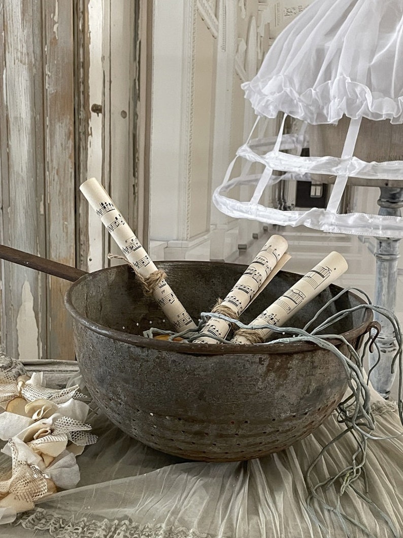 May include: A vintage metal colander with rolled up sheet music inside. The colander is sitting on a white lace tablecloth.