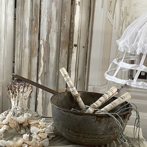 May include: A vintage metal colander with a rustic finish, filled with rolled sheet music and tied with twine. The colander is sitting on a white lace tablecloth with a white, lace-trimmed, decorative object in the foreground.