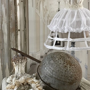 May include: A vintage metal colander with a long handle, sitting on a white lace tablecloth with a white lace crinoline in the background.