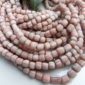 Könnte beinhalten: Eine Strähne aus rosa und weißen, gestreiften Glasperlen. Die Perlen sind klein und haben eine leicht unregelmäßige Form.
