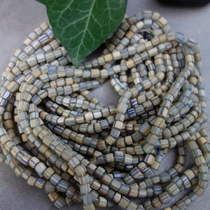 Könnte beinhalten: Eine Schnur kleiner, quadratischer Glasperlen. Die Perlen sind eine Mischung aus hellblau, beige und weiß mit dünnen blauen und goldenen Streifen.