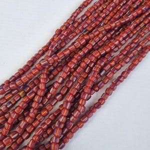 May include: A strand of red, white, and blue glass beads. The beads are small and cylindrical, with a slightly rounded shape. The beads are strung together on a clear thread.