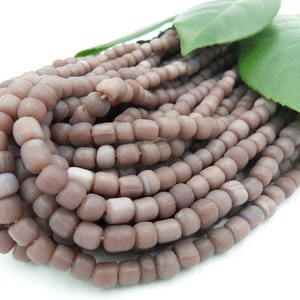 Könnte beinhalten: Eine Strähne aus hellbraunen Glasperlen mit leicht schimmerndem Finish. Die Perlen sind klein und rund und liegen lose in einem Haufen.