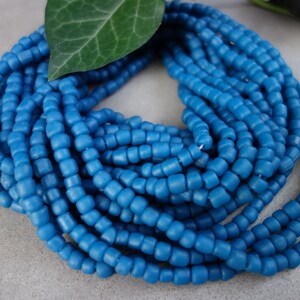 Può includere: Primo piano di una collana di perline di vetro blu. Le perline sono piccole e rotonde, e sono infilate su un filo trasparente. Le perline sono disposte in un motivo circolare, e sono tutte della stessa dimensione e forma.