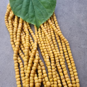 Könnte beinhalten: Eine Sammlung von Strängen gelb getönter, quadratisch geformter Perlen. Ein großes grünes Blatt liegt auf den Perlen. Die Perlen sind auf einer grauen Oberfläche angeordnet. Die Perlen scheinen aus Holz zu sein.