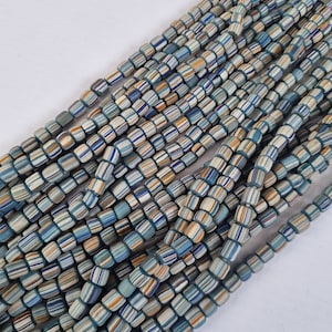 Könnte beinhalten: Eine Strähne aus blauen, weißen und orangefarbenen, gestreiften Glasperlen. Die Perlen sind zylindrisch und haben eine leicht abgerundete Form.