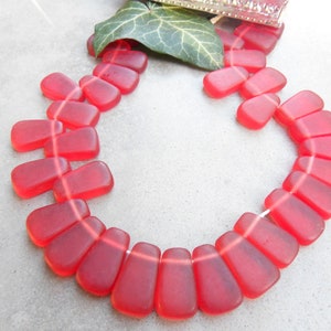 May include: A strand of red glass beads, each bead is shaped like a teardrop with a flat top and a rounded bottom. The beads are strung on a clear thread.