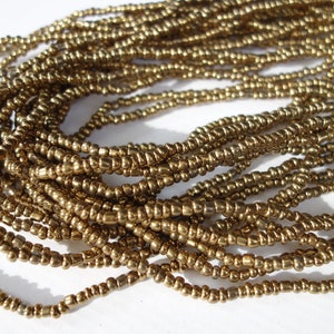 Puede incluir: Primer plano de un montón de cuentas doradas. Las cuentas son pequeñas y redondas, y están dispuestas en un patrón aleatorio.