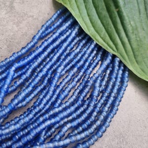 Può includere: Un filo di perline di vetro blu chiaro. Le perline sono piccole e rotonde, e hanno una finitura leggermente opaca.