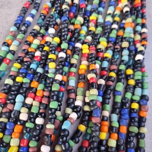 Könnte beinhalten: Nahaufnahme einer mehrfarbigen Perlenkette mit schwarzen Perlen. Die Kette besteht aus kleinen, runden Perlen in verschiedenen Farben, darunter Rot, Orange, Gelb, Grün, Blau und Weiß.