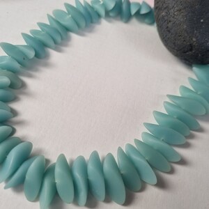 Può includere: Una collana di perline di vetro blu chiaro a forma di lacrima. Le perline sono infilate per formare una collana.