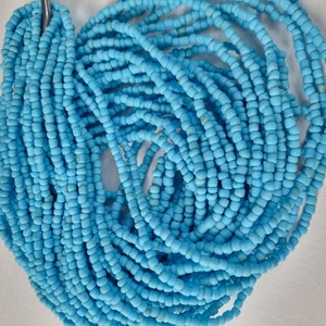 Op de afbeelding: Een verzameling lichtblauwe zaadkralen, aan elkaar geregen, waardoor een wirwar ontstaat, maar toch geordend. De kralen zijn klein, cilindrisch en uniform van grootte, waarschijnlijk voor het maken van sieraden.
