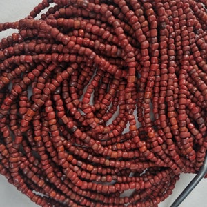 Può includere: Un filo di perline di pietre preziose rosse. Le perline sono piccole e rotonde e sono infilate su un filo sottile. Le perline sono di un colore rosso intenso e hanno una texture leggermente ruvida.