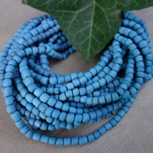 Può includere: Un filo di perline di legno blu chiaro, disposte in cerchio, con una foglia verde dietro le perline.