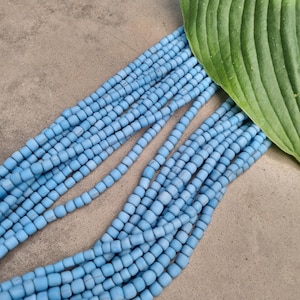 Könnte beinhalten: Eine Reihe von hellblauen quadratischen Perlen, die in Reihen angeordnet sind, vor einem grauen Hintergrund. Ein grünes Blatt ist teilweise in der oberen rechten Ecke des Bildes sichtbar.