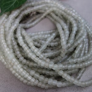 Könnte beinhalten: Eine Strähne aus undurchsichtigen weißen Glasperlen. Die Perlen sind klein und rund und auf einem durchsichtigen Faden aufgereiht.