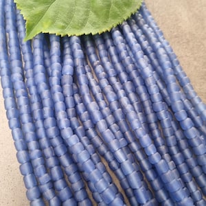 Könnte beinhalten: Nahaufnahme von mehreren Strängen hellblauer Perlen. Die Perlen sind zylindrisch mit abgerundeten Kanten. Ein großes grünes Blatt befindet sich in der oberen linken Ecke. Die Perlen werden wahrscheinlich für die Schmuckherstellung oder andere Bastelarbeiten verwendet.