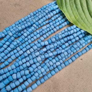 Könnte beinhalten: Eine Strähne aus hellblauen Glasperlen, jede Perle ist leicht abgerundet und hat eine matte Oberfläche. Die Perlen sind in Reihen angeordnet und bilden ein strukturiertes Muster.