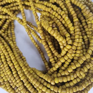 Può includere: Primo piano di una collezione di perline gialle. Le piccole perline cilindriche sono infilate, formando più fili. Il colore è un giallo tenue con variazioni di tonalità, che suggeriscono un materiale naturale. Le perline sono probabilmente per la creazione di gioielli.