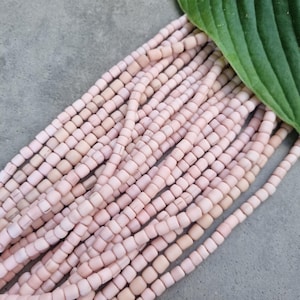 Può includere: Un filo di perline quadrate rosa pallido, in legno, disposte a cascata su una superficie grigia.