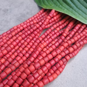 Può includere: Un filo di perline rosso vivo, probabilmente in argilla o ceramica, disposte in file. Le perline sono piccole e di dimensioni uniformi, creando un motivo visivamente accattivante.