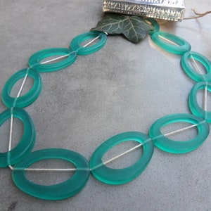 Könnte beinhalten: Eine Strähne aus ovalen Perlen in Türkisgrün mit einer weißen Schnur, die durch die Mitte jeder Perle verläuft.