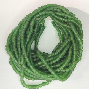 Op de afbeelding: Een streng groene glazen kralen. De kralen zijn klein, rechthoekig en hebben een licht doorschijnend uiterlijk. De kralen zijn aan elkaar geregen en vormen een ketting of decoratief element. De kleur is een levendig, medium groen.