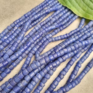 Könnte beinhalten: Eine Strähne blauer Glasperlen, jede Perle ist quadratisch mit abgerundeten Kanten. Die Perlen sind in Reihen angeordnet und bilden ein strukturiertes Muster.