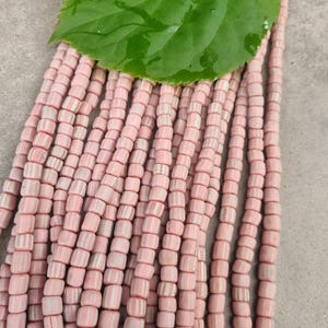 May include: A collection of pink and white striped beads, with a large green leaf on top. The beads are cylindrical and appear to be made of glass or ceramic. The beads are strung together, creating a textured and colourful display.