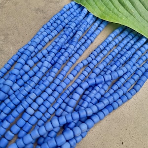 Pode incluir: Um fio de contas de vidro azul claro, cada conta tem formato quadrado e acabamento fosco.