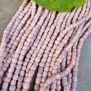 Op de afbeelding: Een streng roze en wit gestreepte glazen kralen. De kralen zijn klein en rond en aan elkaar geregen op een doorzichtige draad.