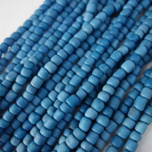 Pode incluir: Um fio de contas quadradas de cor azul claro. As contas são de madeira e têm um acabamento fosco.