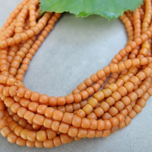 Könnte beinhalten: Eine Strähne orangefarbener Glasperlen, jede Perle hat eine kleine, abgerundete quadratische Form.