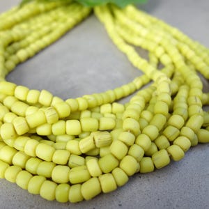 Könnte beinhalten: Nahaufnahme einer langen Schnur gelber Glasperlen. Die Perlen sind klein und rund und zu einer durchgehenden Schleife aufgereiht.