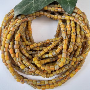 May include: A close-up of a strand of yellow, orange, and white striped glass beads. The beads are arranged in a circle and are stacked on top of each other.